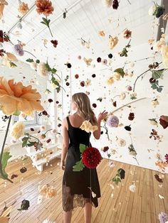 a woman standing in front of a flower filled room with flowers floating from the ceiling