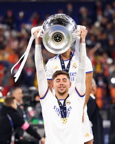 two soccer players hold up the trophy in front of their heads as they look on