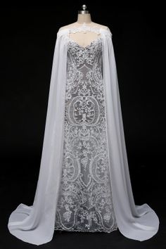 a white wedding gown on display with a cape over the shoulders and an elaborate lace appliqued top