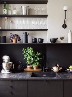 a kitchen with black cabinets and shelves filled with pots, pans, and plants