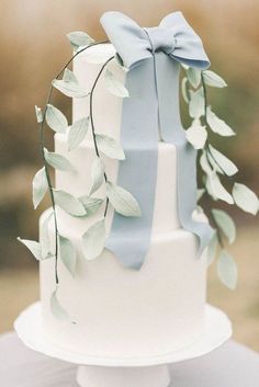 a white cake with blue ribbon and green leaves