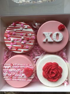 four decorated cupcakes in a box with pink and red icing on them