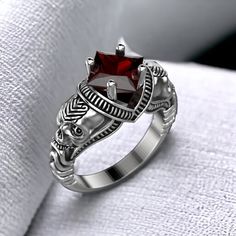 a silver ring with a red stone in the center on top of a white cloth