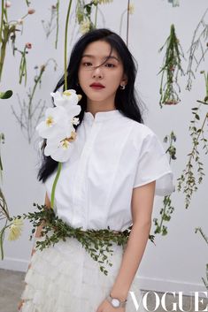 a woman with long black hair wearing a white dress and holding a flower in her hand