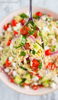 a spoon full of pasta salad with tomatoes and cucumbers