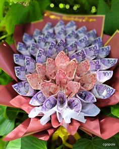 an origami flower made out of money sitting on top of leaves