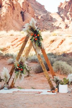 a wedding arch decorated with flowers and feathers in the middle of an outdoor desert setting