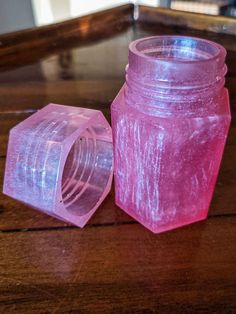 a pink plastic jar sitting on top of a wooden table next to a small container