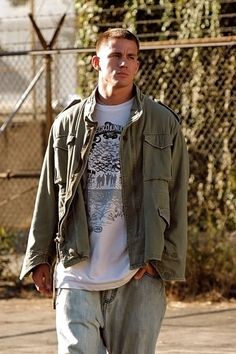 a young man walking down the street with his hands in his pockets and wearing an army green jacket