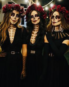 three women with skeleton makeup and flowers on their heads are standing in front of string lights