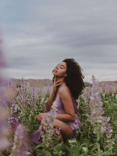 a woman sitting in a field of flowers with her eyes closed and hands to her face