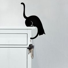 a black cat on top of a white cabinet with keys in it's mouth