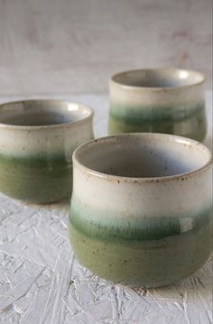 three green and white cups sitting on top of a tablecloth covered table next to each other