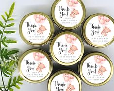 four tins with thank you for baby shower favors in pink and gold, sitting next to a potted plant