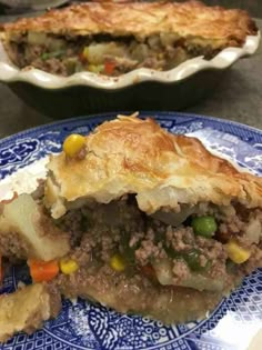 a meat pie on a blue and white plate next to another pie in a dish