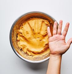 a person holding their hand up to a bowl with food in it on a white surface