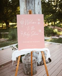 a welcome to the baby shower sign sitting on top of a wooden easel next to a tree