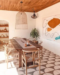 a dining room table and chairs with artwork on the wall behind it, in front of a potted plant