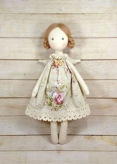 a small doll is wearing a dress with flowers and laces on the bottom, standing against a wooden wall