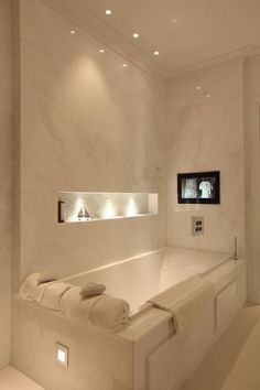 a large white bath tub sitting next to a tv mounted on the side of a wall