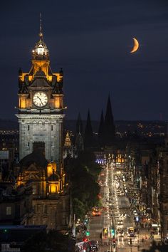 a clock tower in the middle of a city at night with traffic passing below it