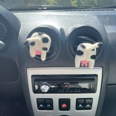 two stuffed cows are placed in the center console of a car with radio and dashboard controls