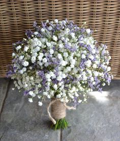 a bouquet of white and purple flowers sitting on top of a stone floor next to a wicker basket