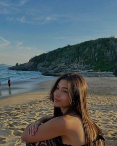 a woman sitting on top of a sandy beach next to the ocean with her arms crossed