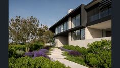 an exterior view of a modern home surrounded by greenery and shrubs, with stairs leading up to the front door