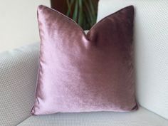 a purple velvet pillow sitting on top of a white couch next to a potted plant