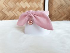 a pink bow tie on top of a white headband with a gold bell charm