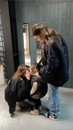 a woman and two children are looking at something on the ground in front of a mirror