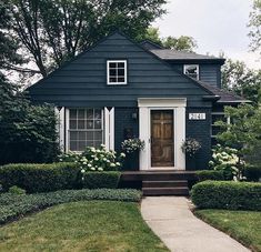 a blue house with white trim and flowers on the front door is surrounded by hedges