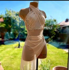 a dress on display in front of a window with grass and bushes behind the mannequin