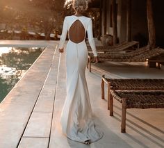 a woman in a long white dress is walking by the pool with her back to the camera