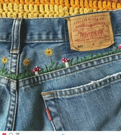 the back pocket of a pair of jeans with flowers and grass embroidered on it, next to a yellow knitted hat