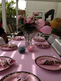 the table is set with pink and black plates, napkins, and flowers in a vase