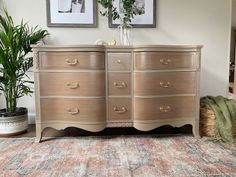 an old dresser with two pictures on the wall and a potted plant next to it