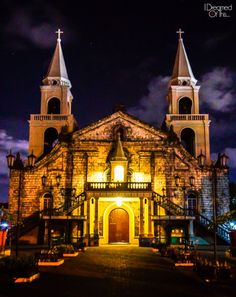 an old church lit up at night with clouds in the sky and lights shining on it