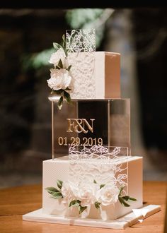 a three tiered wedding cake with white flowers on the side and initials on top