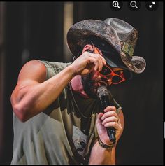 a man with a hat and sunglasses on holding a microphone to his face while singing