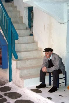 an old man sitting on a chair in front of some stairs