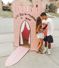 a man and woman kissing in front of a fake pink castle with writing on it