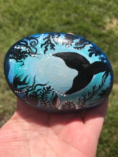 a hand holding a painted rock with a dolphin on it