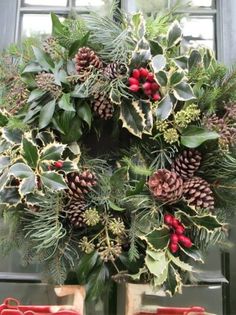 a christmas wreath with pine cones, holly and berries in front of a glass door