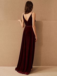 a woman in a long velvet dress standing against a wall with her back to the camera