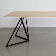 a wooden table sitting on top of a cement floor next to a white wall and black metal frame