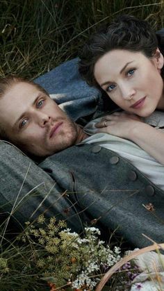 a man and woman laying on top of each other in the grass next to flowers