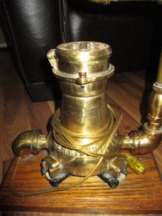 an old fashioned brass lamp is sitting on a wooden stand with pipes and wires attached to it