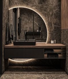 a bathroom with marble walls and flooring is seen in this image, it has a circular mirror over the sink